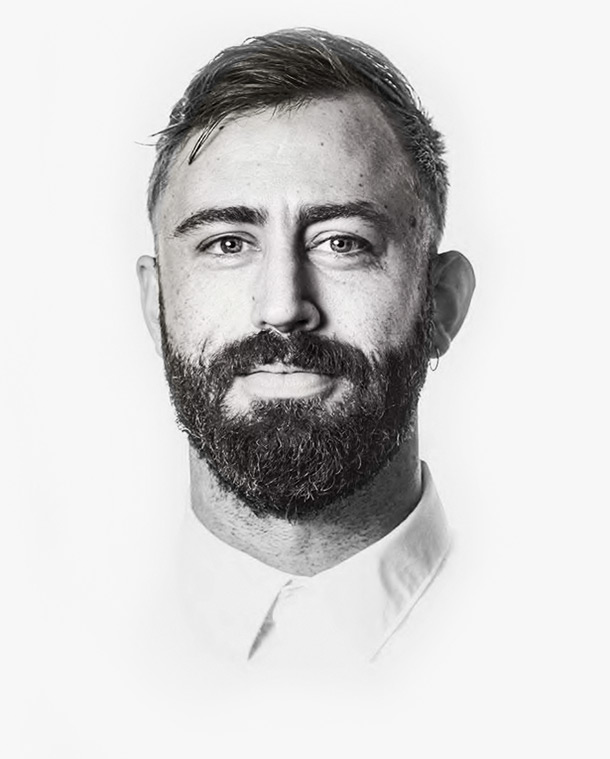 Portrait of a man with short hair, a thick beard, and a calm expression, photographed in black and white against a clean white background.